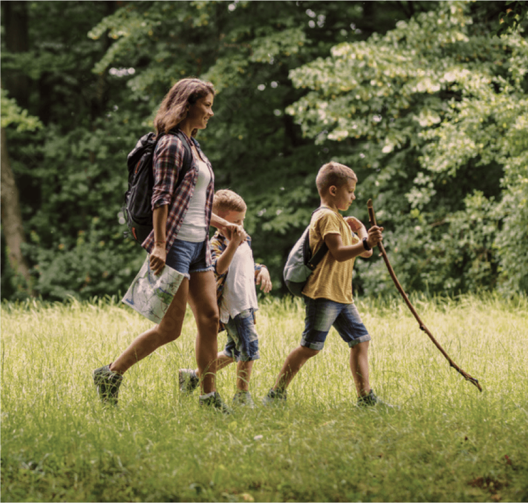 Mother and two young boys hiking through a sunlit forest clearing on a nature journey