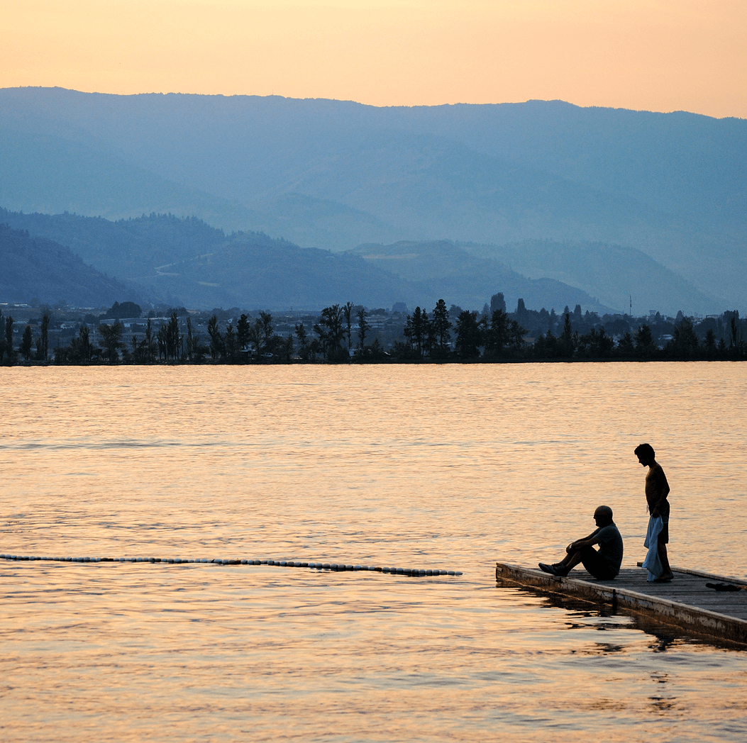 Two people on a dock at sunset overlooking Osoyoos Lake and mountain backdrop in British Columbia